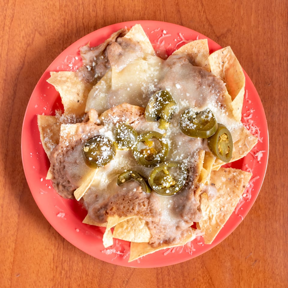 Nachos with melted cheese, refried beans, pickled jalapeños, and grated cheese on a red plate.