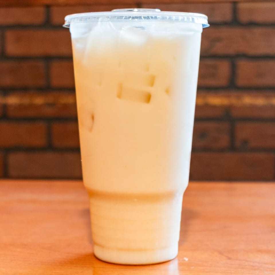 Iced Thai tea in a clear plastic cup with a lid, on a wooden table.