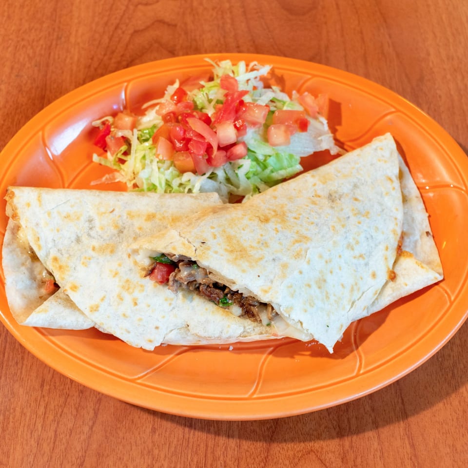 A large quesadilla filled with meat and cheese, served with a side of shredded lettuce and diced tomatoes.