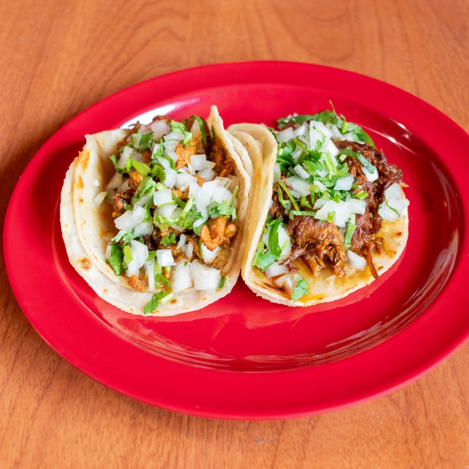 Two delicious tacos with meat, onions, and cilantro on a vibrant red plate.