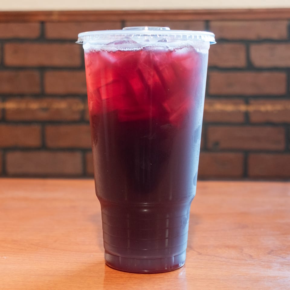 A clear plastic cup filled with a dark red iced beverage sits on a wooden table.