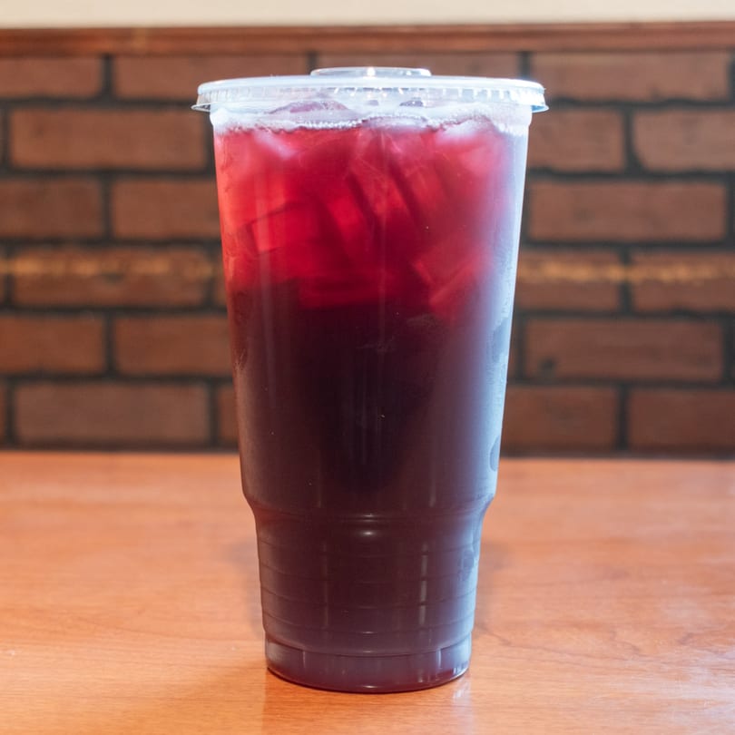 A clear plastic cup filled with a dark red iced beverage sits on a wooden table.