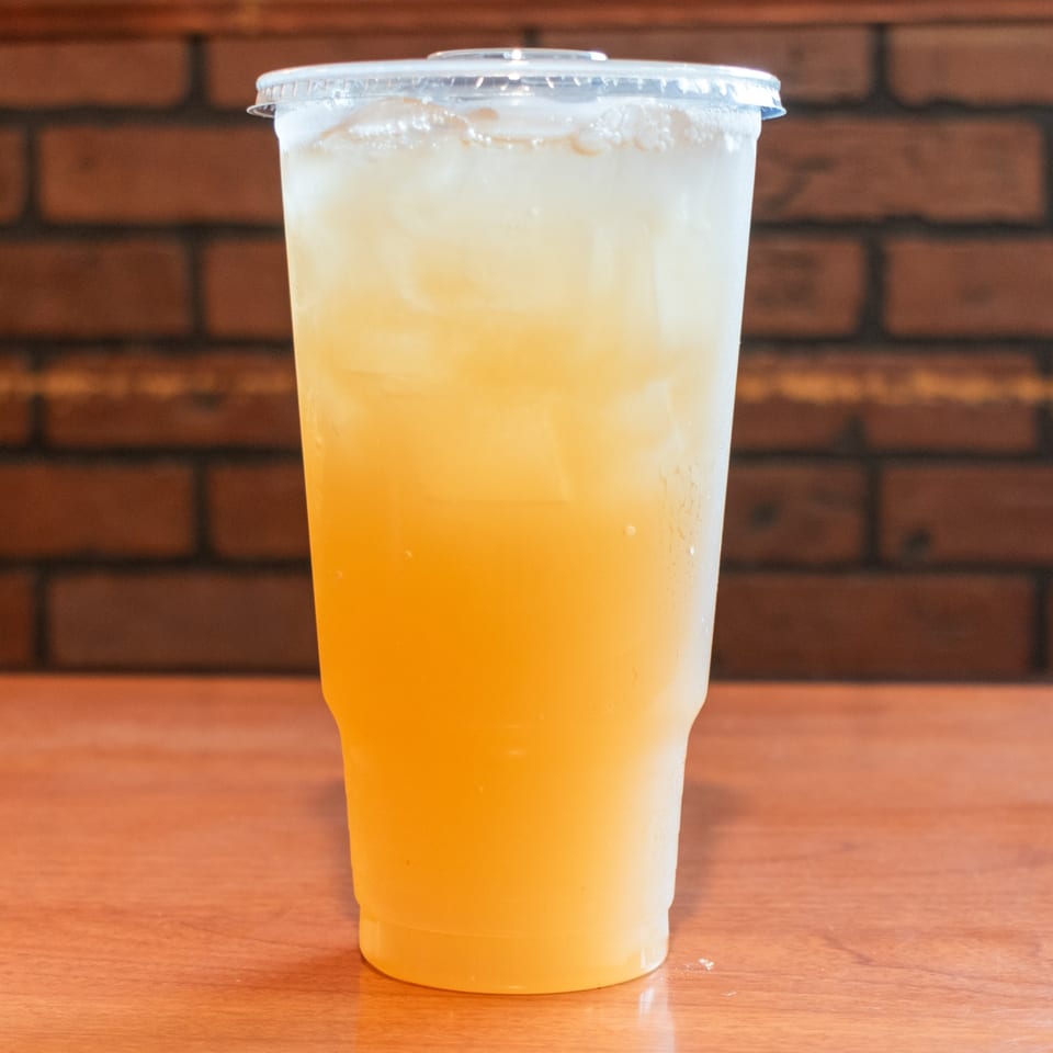 A tall, clear plastic cup filled with a golden-yellow iced beverage sits on a wooden table.