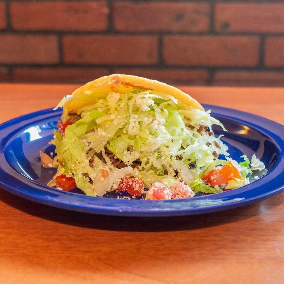 A crispy taco shell overflowing with seasoned meat, shredded lettuce, diced tomatoes, and crumbled cheese.